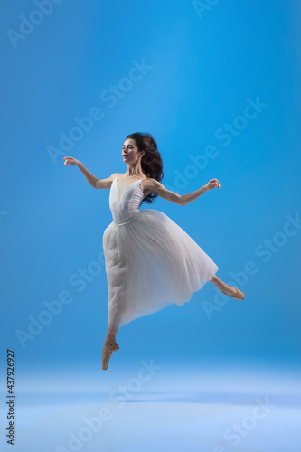 Young and graceful ballet dancer isolated on blue studio background. Art, motion, action, flexibility, inspiration concept.