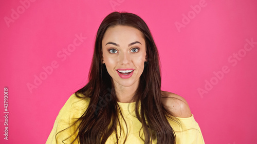 positive young adult woman in yellow blouse looking at camera isolated on pink