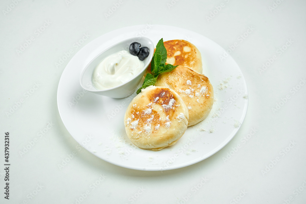 Ukrainian sweet dish - cottage cheese pancakes with sour cream on a white plate on a white background. Sweet syrniki