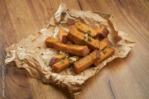 Appetizing snack with beer - rye croutons with garlic and herbs on parchment on a wooden background.