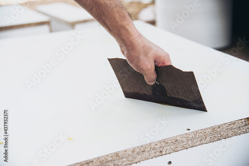 Carpenter making wooden built-in furniture putting rubber glue to attach laminate surface