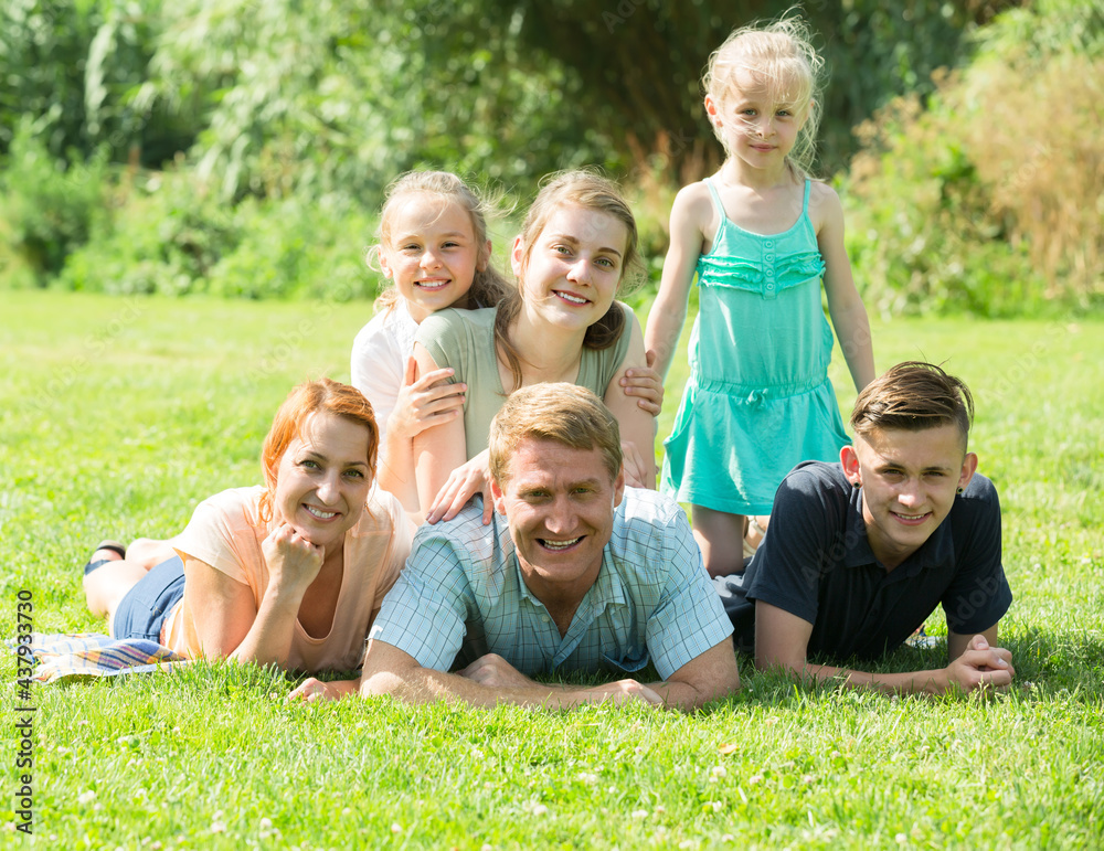 happy large family with four different age children resting on the green meadow in park on summer day.