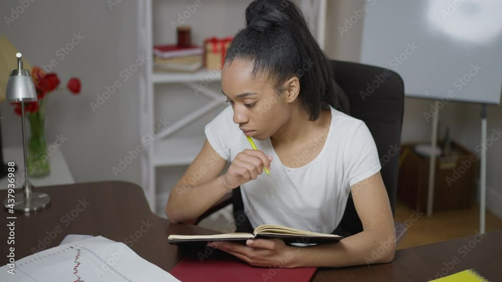 Concentrated thoughtful woman looking at business graph planning strategy idea sitting at table with sketchpad. Portrait of African American consultant examining paperwork in home office indoors Concentrated thoughtful woman looking at business graph planning strategy idea sitting at table with sketchpad. Portrait of African American consultant examining paperwork in home office indoors