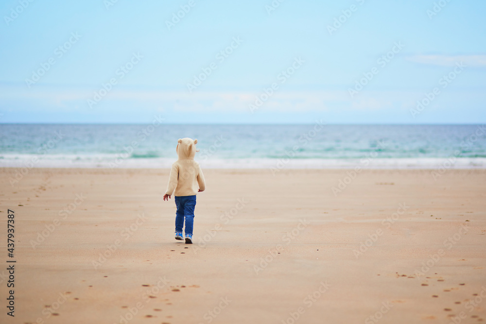 Adorable toddler girl on the sand beach at Atlantic coast of Brittany, France Adorable toddler girl on the sand beach at Atlantic coast of Brittany, France