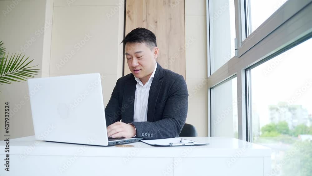 young asian business man sitting in the office talking online via webcam, looking at laptop. Male in a formal suit, an employee or manager waving his hand, happy talking on a video call indoors young asian business man sitting in the office talking online via webcam, looking at laptop. Male in a formal suit, an employee or manager waving his hand, happy talking on a video call indoors