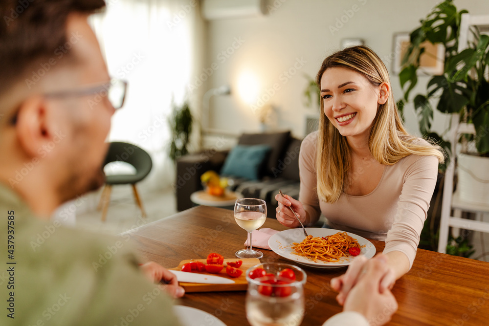 Cheerful couple having romantic time, holding a hand, eating food and drinking a wine.