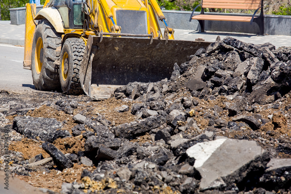 Fototapeta premium special road machinery a tractor with a bucket removes the remains of pieces of asphalt road surface repair work close-up nobody.