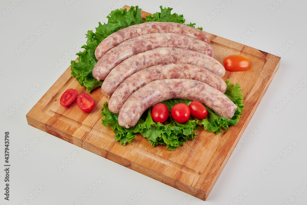 Meat kupatas five pieces with red cherry tomatoes and green lettuce leaves on a rectangular wooden cutting board on a white background.