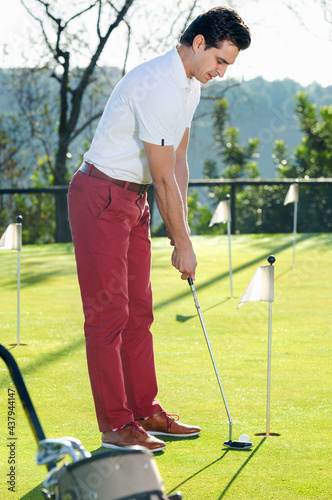 Young glad cheerful positive man preparing to hit ball at golf course