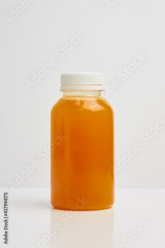 Transparent plastic bottle with a white lid, with orange juice inside on a white background.
