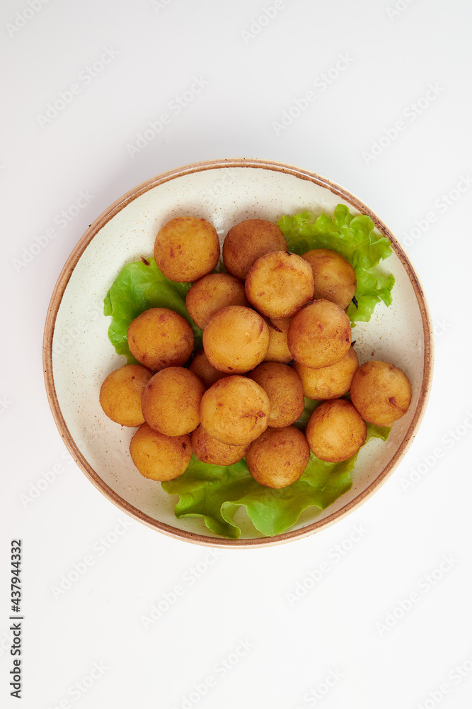 Breaded cheese balls with three green lettuce leaves in a white round plate on a white background. Breaded cheese balls with three green lettuce leaves in a white round plate on a white background.