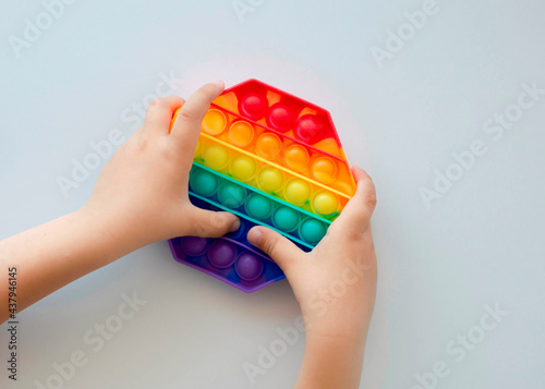 Colorful antistress sensory toy fidget push pop it in kid's hands. Child playing with rainbow pop it,top view.New antistress toy for children and adult