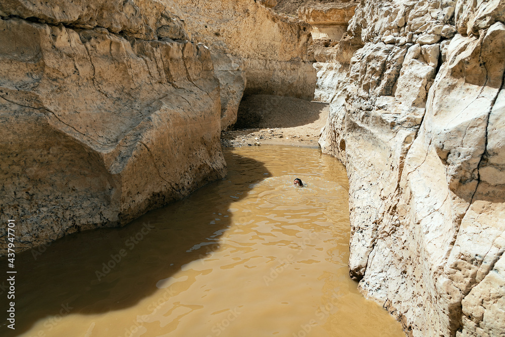 one person playing in a rainpool in the flooded Horseshoe section of the Nahal Nekarot stream in the Makhtesh Ramon crater showing the sheer vertical white limestone canyon walls