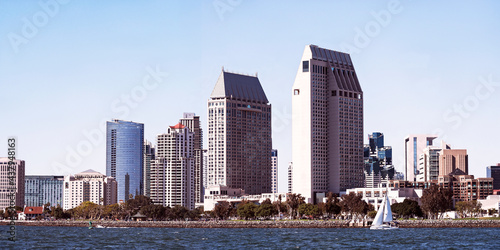 downtown San Diego California skyline showing skyscrapers, hotels and the Embarcadero Marina Park with the San Diego Bay and a single sailboat in the foreground