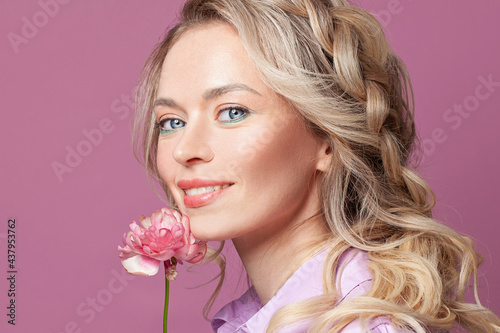 Happy pretty blonde woman with flower smiling on pink, beautiful face close up