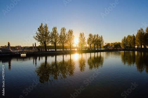 Scenic sunset landscape near embankment in the Taras Shevchenko Park in Ternopil. Sun and trees reflected in the tranquil water. Famous touristic place and romantic travel destination. Ukraine