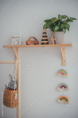 Children's room concept. Environmentally friendly toys. Wooden shelf, wooden typewriter, pyramid and knitted rainbow on a white wall.
