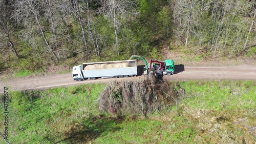 Aerial shot of wood chipper blowing shredded wood into back of a truck. Forest background photo