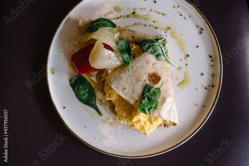 Omelette in lavash with slices of pepper and spinach leafs on a plate
