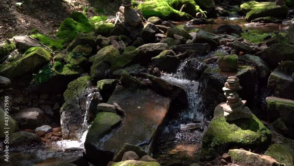 Kleiner Bergbach mit Kaskaden fließt durch moosige Steine an einem gebauten  Steinmännchen