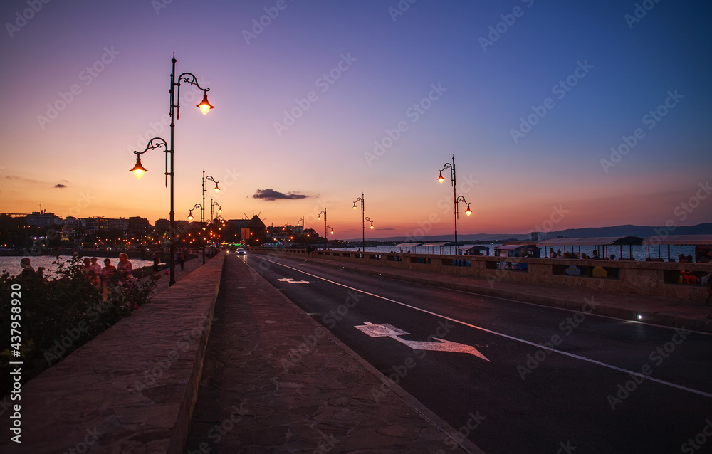 Asphalt road in sea bay leading to old town of Nessebar, Bulgaria, on background of colorful sky