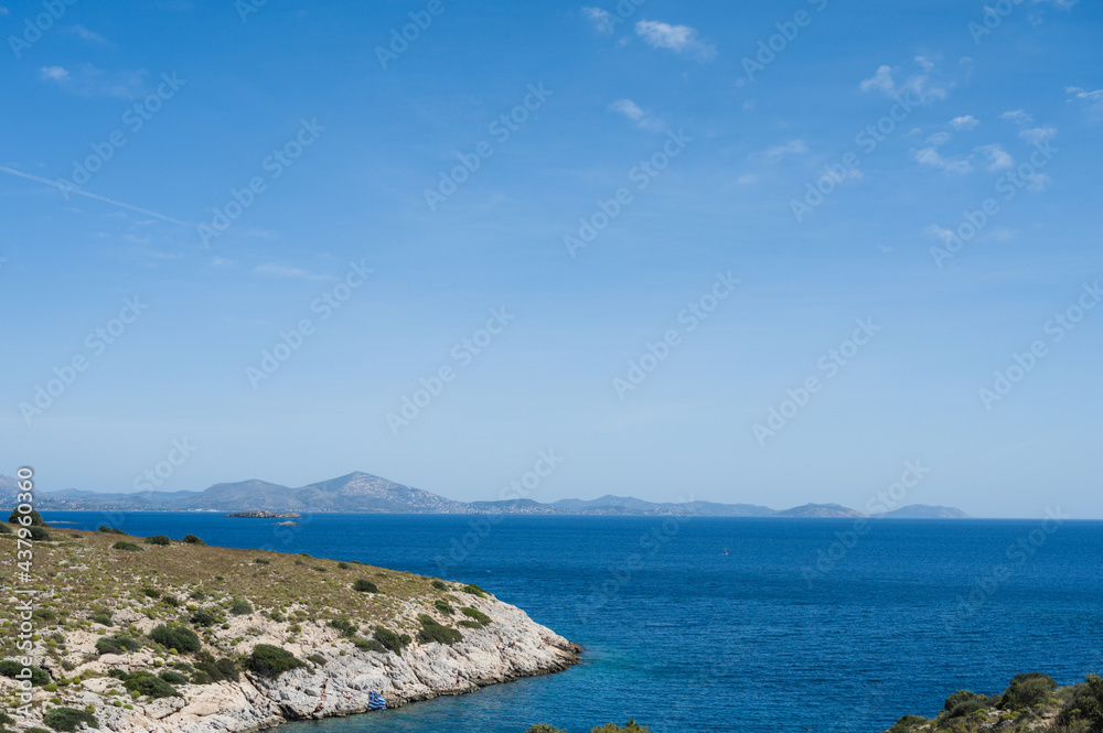Scenic landscape of Aegean sea at sunny summer day. Athens, Greece. Stone shore. Blue sky and water. Silhouette of mountains.