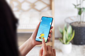 Girl use smart phone for plan a trip. Modern phone app with search tour option. Phone in girl hands. Over the shoulder view