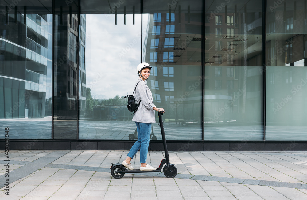 custom made wallpaper toronto digitalSide view of young smiling businesswoman with cycling helmet on her head driving an electrical push scooter