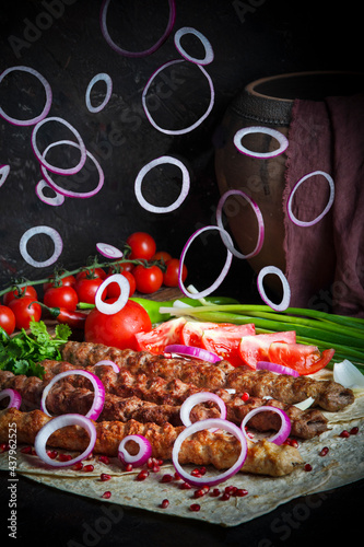 Meat lula kebab served on lavash bread with flying onion rings on foreground. Bbq meat pieces with tomatoes and spring onions. Traditional Caucasian Shashlik
 photo