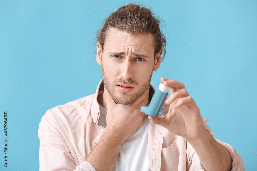 Young man with inhaler having asthma attack on color background
