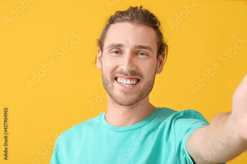 Smiling young man taking selfie on color background © Pixel-Shot