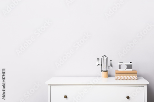 Stylish decor on chest of drawers near light wall