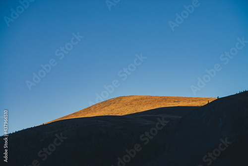 Autumn landscape with dark silhouettes of mountains and vivid beautiful orange mountain top in golden sunlight. Vivid alpine scenery with mountain silhouettes and sunlit gold hill top in autumn colors