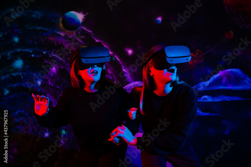Two girls friends in virtual glasses are holding hands in the playroom in neon light