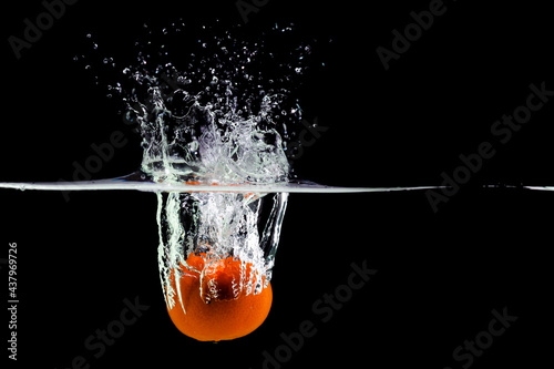 Mandarin falls into water creating spray on a black background, copy space