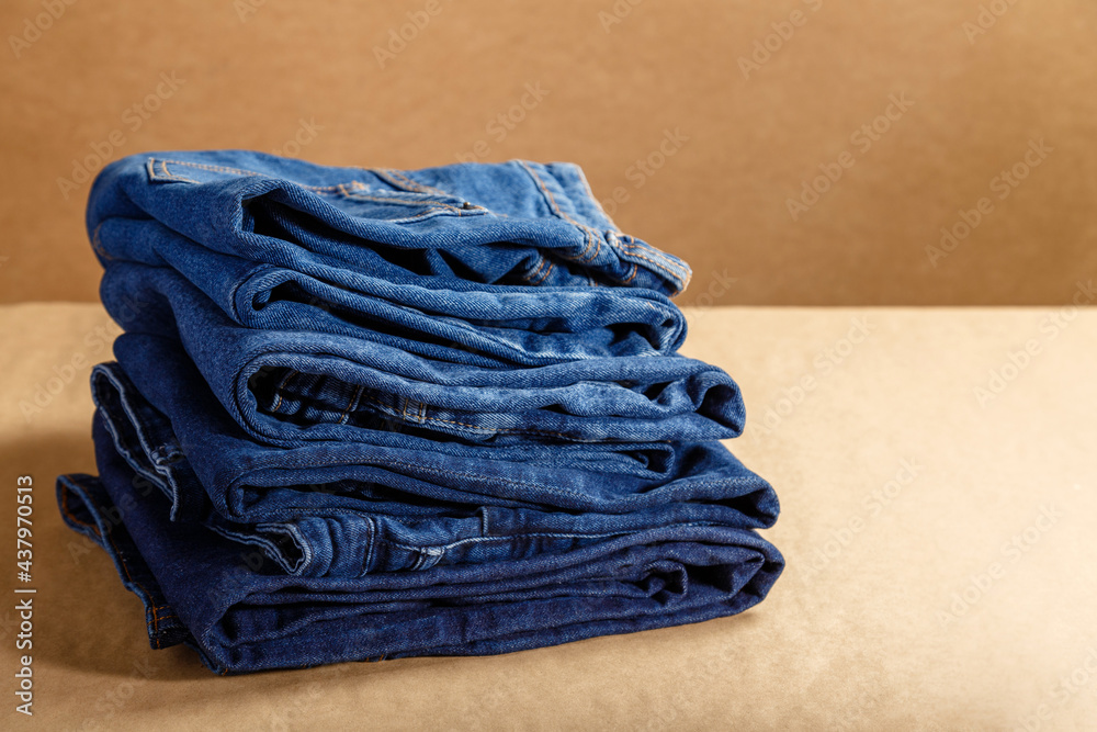 Stack of blue denim clothes. Pile folded blue denim pants in different shades of blue on brown craft background with copy space Stack of blue denim clothes. Pile folded blue denim pants in different shades of blue on brown craft background with copy space