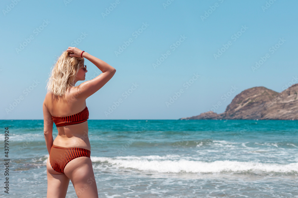 Rear view of woman in swimsuit on the beach looking to the waves on sea. Crete island Greece. Rear view of woman in swimsuit on the beach looking to the waves on sea. Crete island Greece.