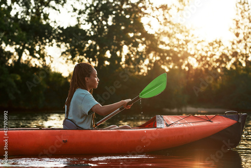 Side view of young woman looking relaxed while kayaking in a lake surrounded by nature on a late summer afternoon