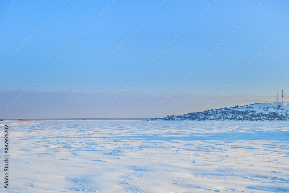 Panorama of a wide frozen river in winter. On the right side you can see a coastal village or town. On the left, you can see the temporal road laid along the snowdrifts Panorama of a wide frozen river in winter. On the right side you can see a coastal village or town. On the left, you can see the temporal road laid along the snowdrifts