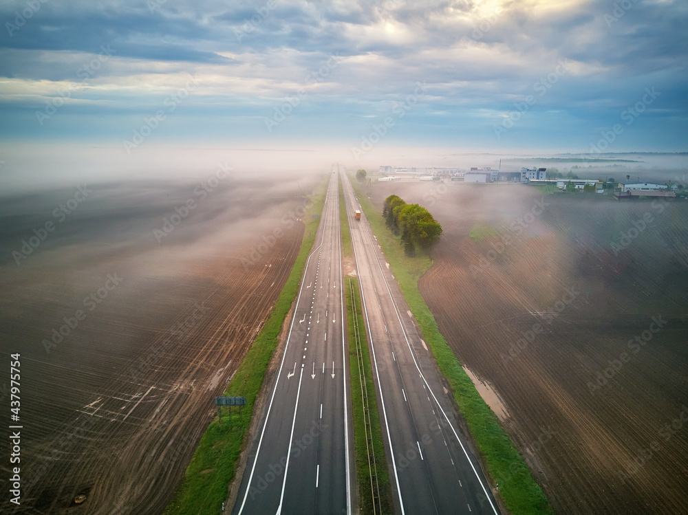Aerial view of a highway covered by fog. Early misty morning. Road in rainy spring summer fields.