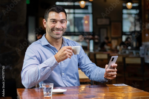 Hombre joven enviando mensaje por el movil mientras toma cafe en una cafeteria moderna photo