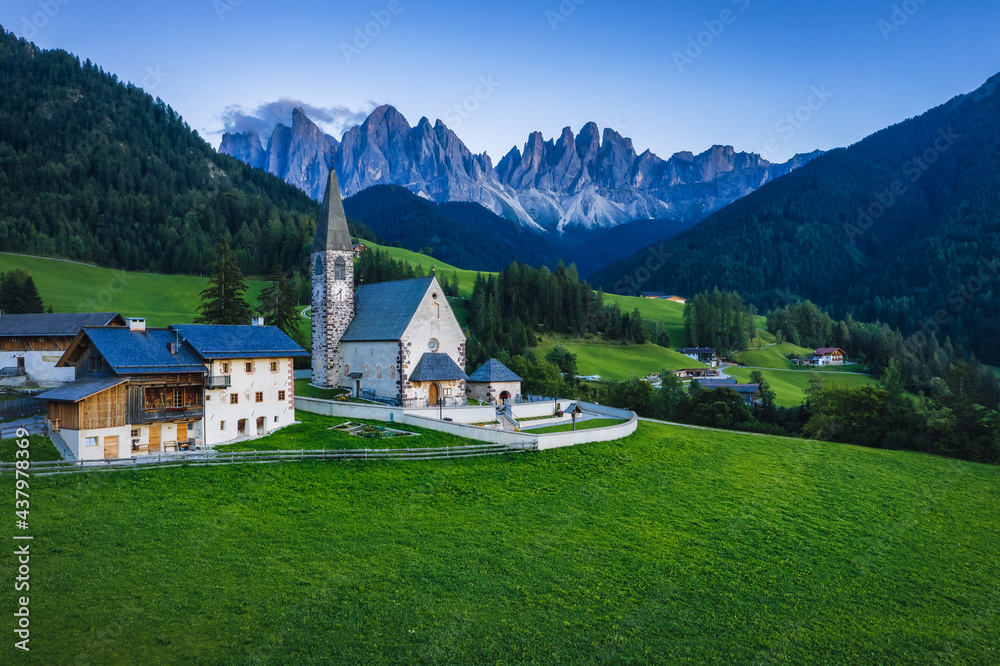 St Magdalena church in Val di Funes valley in evening dusk light, Dolomites, Italy. Furchetta and Sass Rigais mountain peaks in background