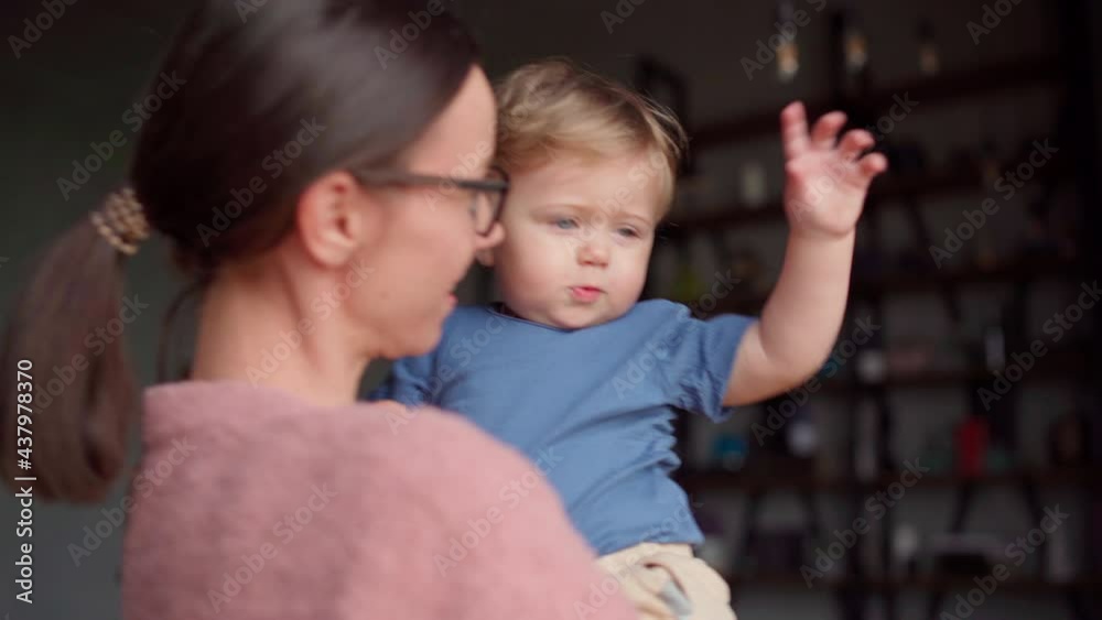 Loving young mother holding cute baby son in her arms, playing with him, tossing gently. Curious baby boy pointing at something interesting, mom talking to him, explaining things and kissing Loving young mother holding cute baby son in her arms, playing with him, tossing gently. Curious baby boy pointing at something interesting, mom talking to him, explaining things and kissing