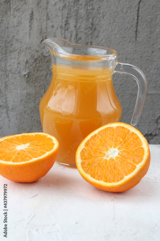 concept of healthy food. Fresh orange juice in the glass jug and juicy fresh oranges on a neutral vertical background concept of healthy food. Fresh orange juice in the glass jug and juicy fresh oranges on a neutral vertical background