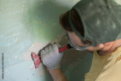Caucasian man removing old paint with scraper tool.