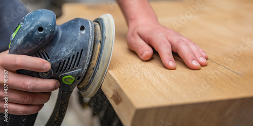 A carpenter works in a workshop. Joiner's grinders, furniture manufacturing. A carpenter is grinding a wooden part with an electric sander. place to insert text photo