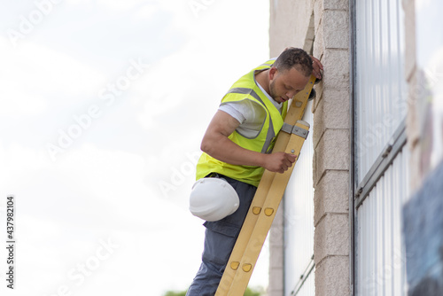 telecommunications technician standing at the top of a ladder without a safety helmet on and looking down.