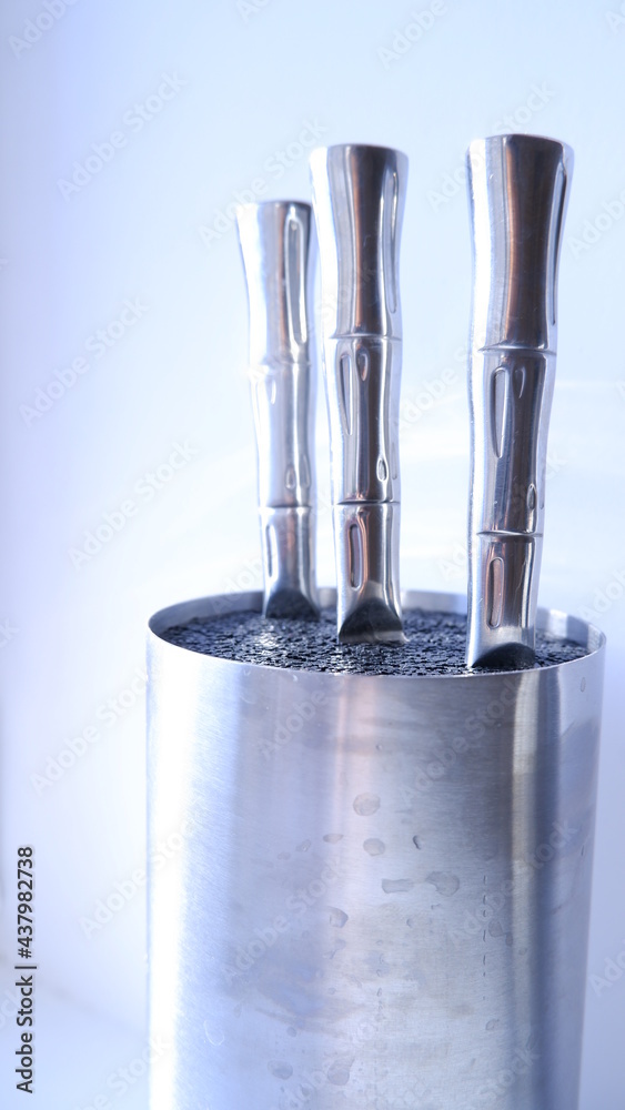 A set of kitchen knives in a metal block of knives with on a white background. Metal beautiful knife handles in a metal round knife block. Close up. Blue, white, silver color A set of kitchen knives in a metal block of knives with on a white background. Metal beautiful knife handles in a metal round knife block. Close up. Blue, white, silver color