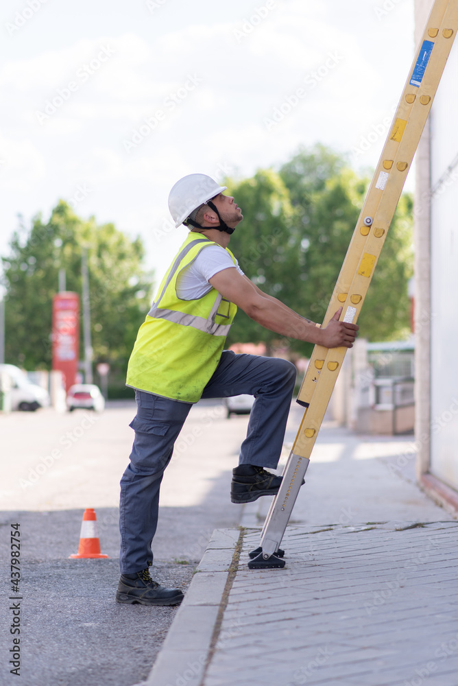 telecommunications technician with one foot on the ground and the other on a ladder with helmet, safety boots and reflective vest.