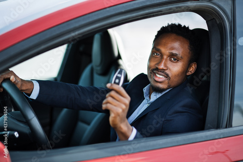 African american businessman in suit sitting inside his luxury electric car with keys in hands. Handsome man looks satisfied with successful purchase. Concept of eco friendly vehicle. © sofiko14
